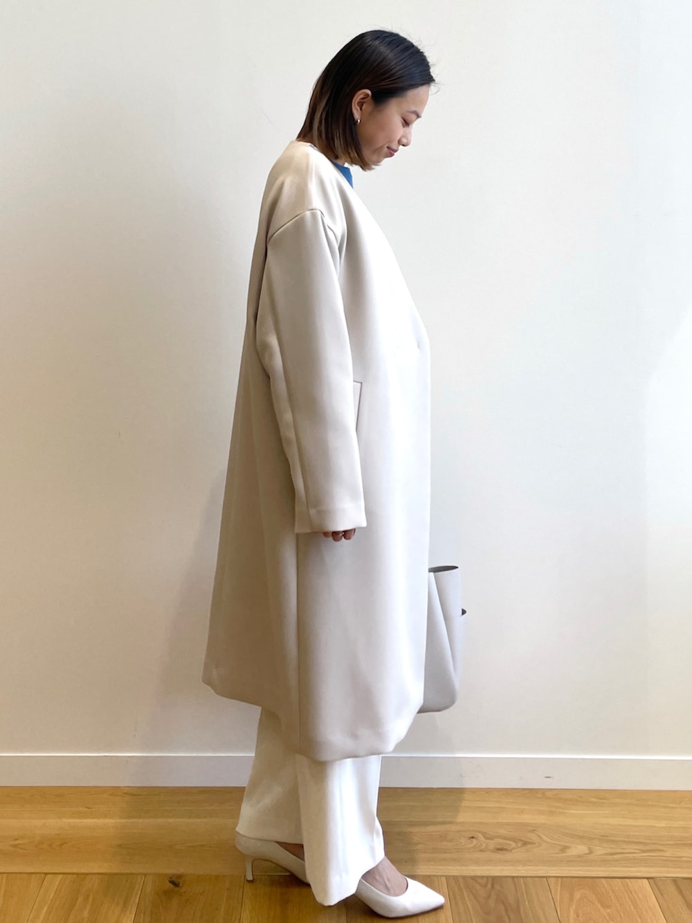 ホワイト系のノーカラーコート、ブルー系のニット/セーター、ホワイト系のその他パンツを着用したレディースの春コーディネートの2枚目の写真