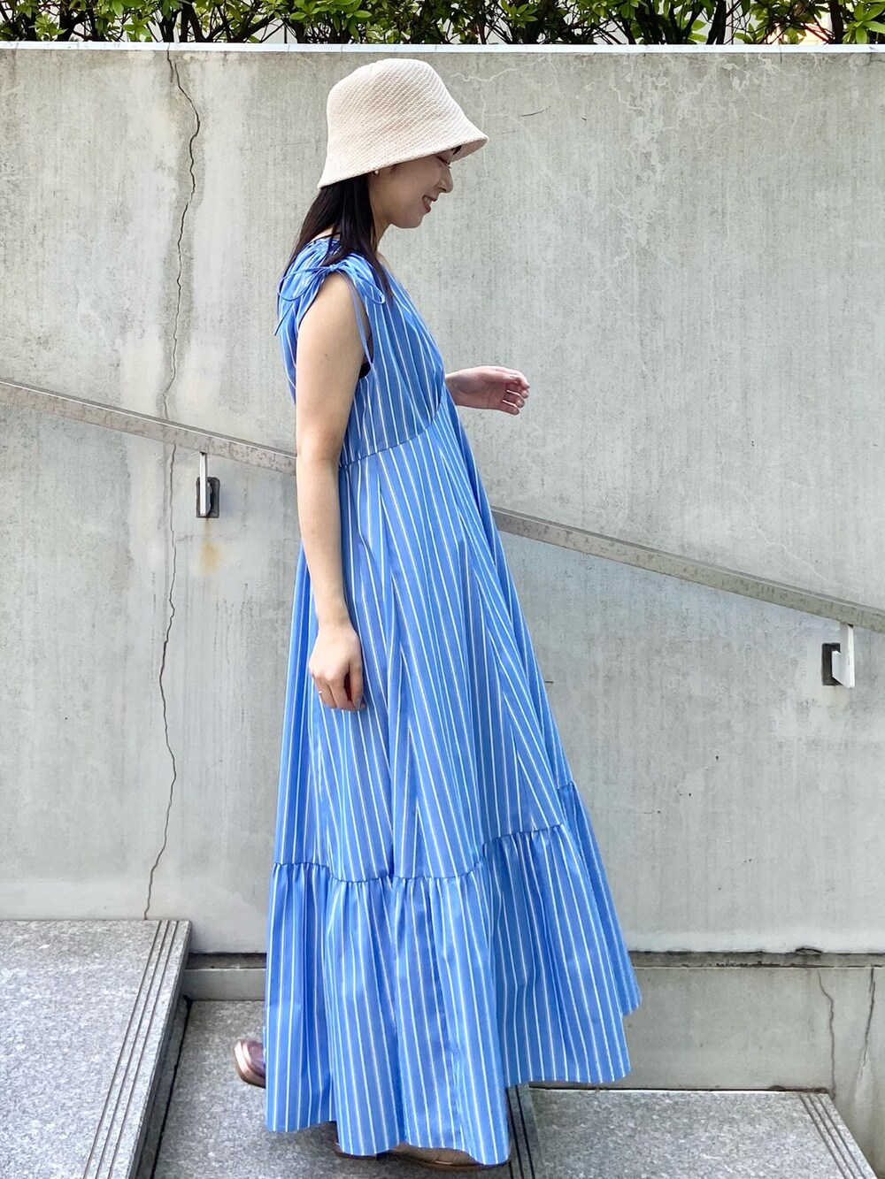 ブルー系のワンピース、ゴールド系のサンダル、ホワイト系のハットを着用したレディースの夏コーディネートの2枚目の写真