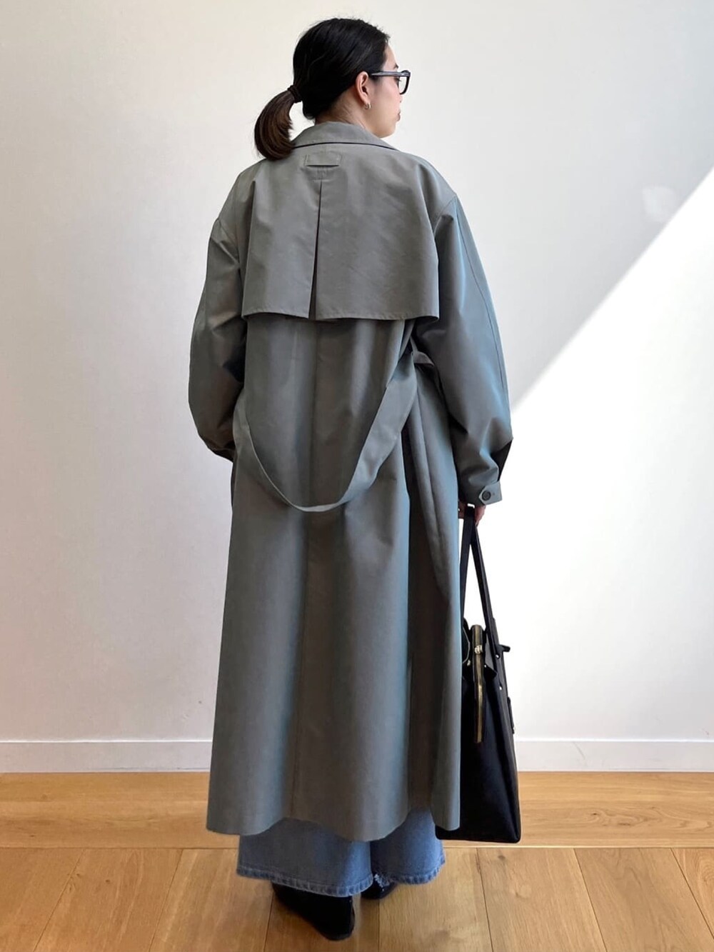 グリーン系のトレンチコート、ブルー系のデニムパンツ、ブラック系のトートバッグを着用したレディースの冬コーディネートの2枚目の写真