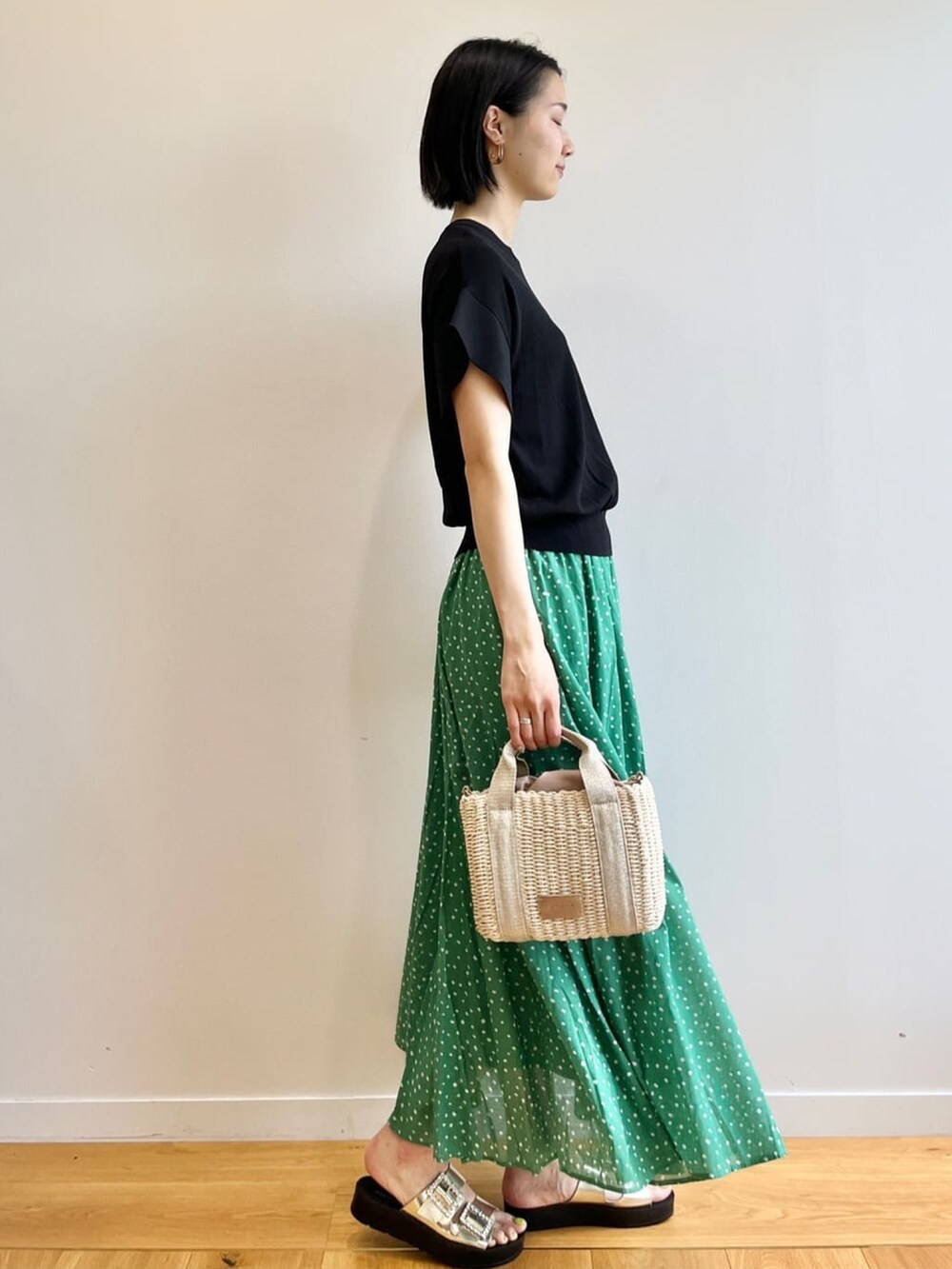 ブラック系のニット/セーター、グリーン系のスカート、ゴールド系のサンダルを着用したレディースの春コーディネートの3枚目の写真