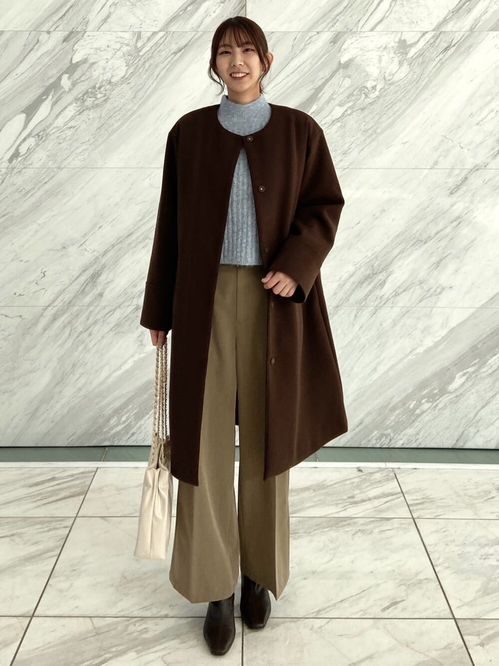 ブラウン系のノーカラーコート、ブラウン系のその他パンツ、ブルー系のニット/セーターを着用したレディースの秋コーディネートの2枚目の写真
