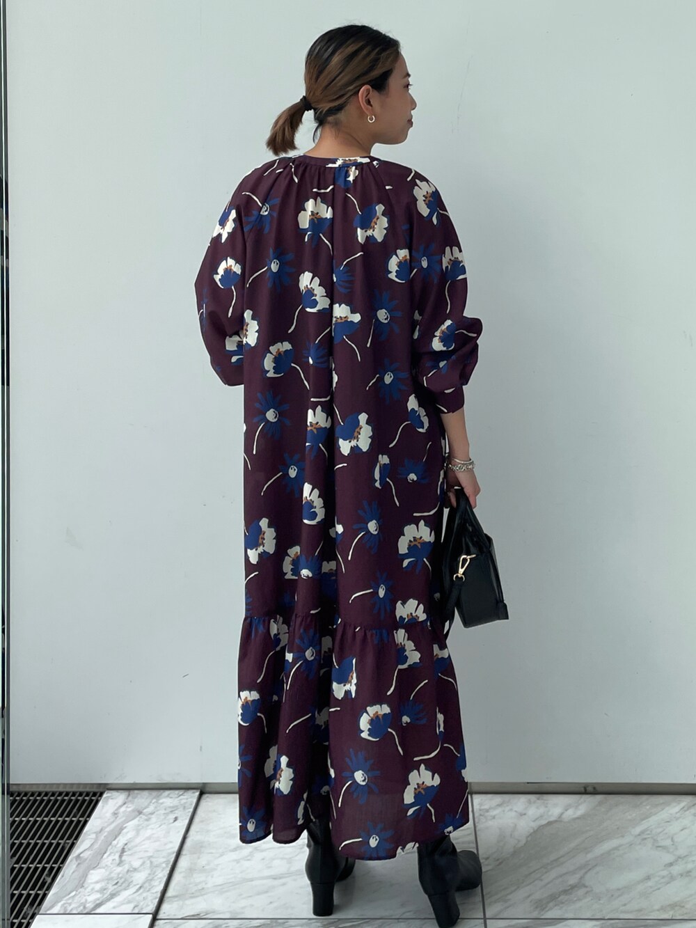 パープル系のワンピース、ブラック系のショルダーバッグ、ブラック系のブーツを着用したレディースの夏コーディネートの2枚目の写真