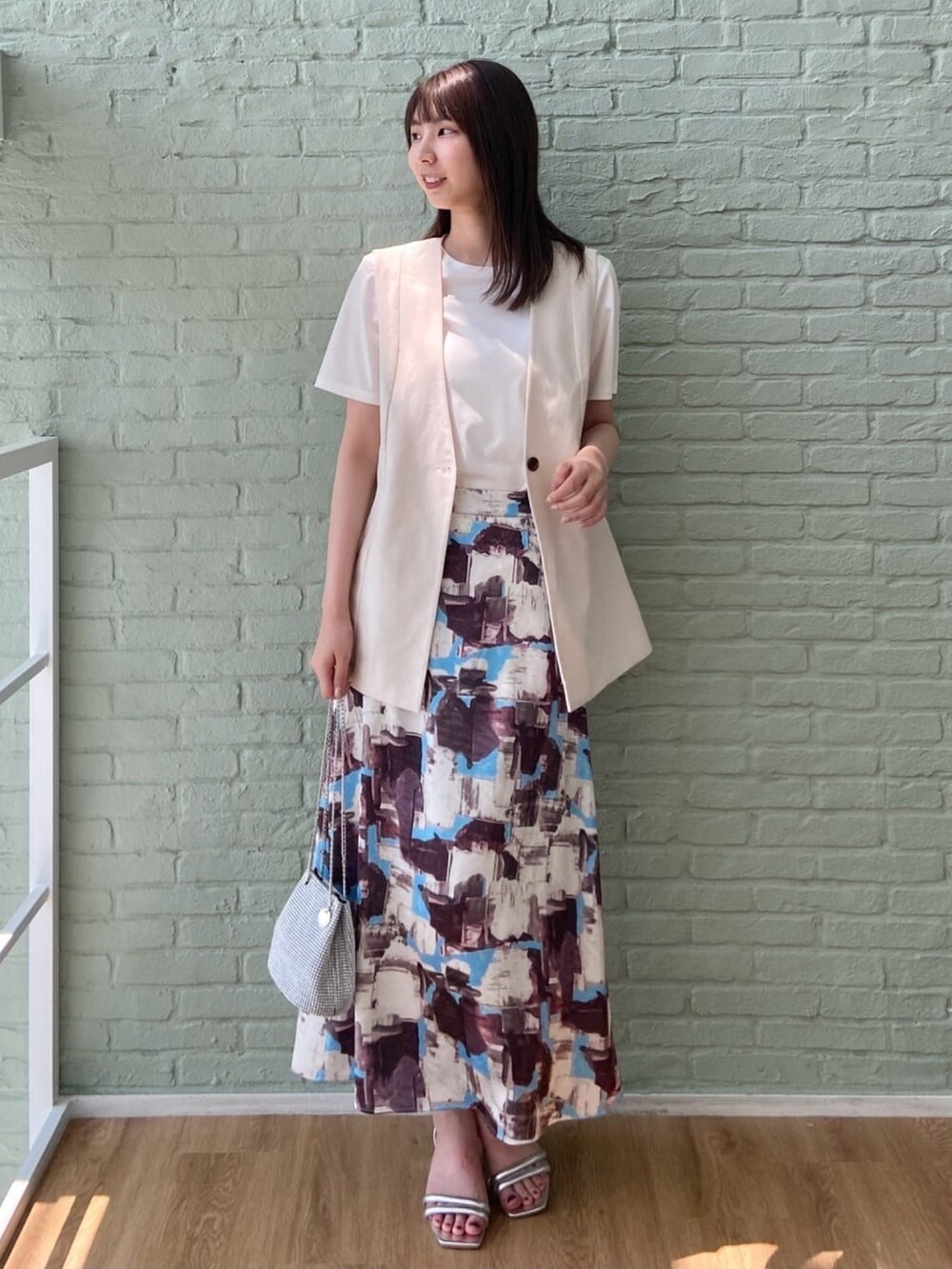 ベージュ系のベスト、ホワイト系のTシャツ/カットソー、レッド系のスカートを着用したレディースの夏コーディネートの2枚目の写真