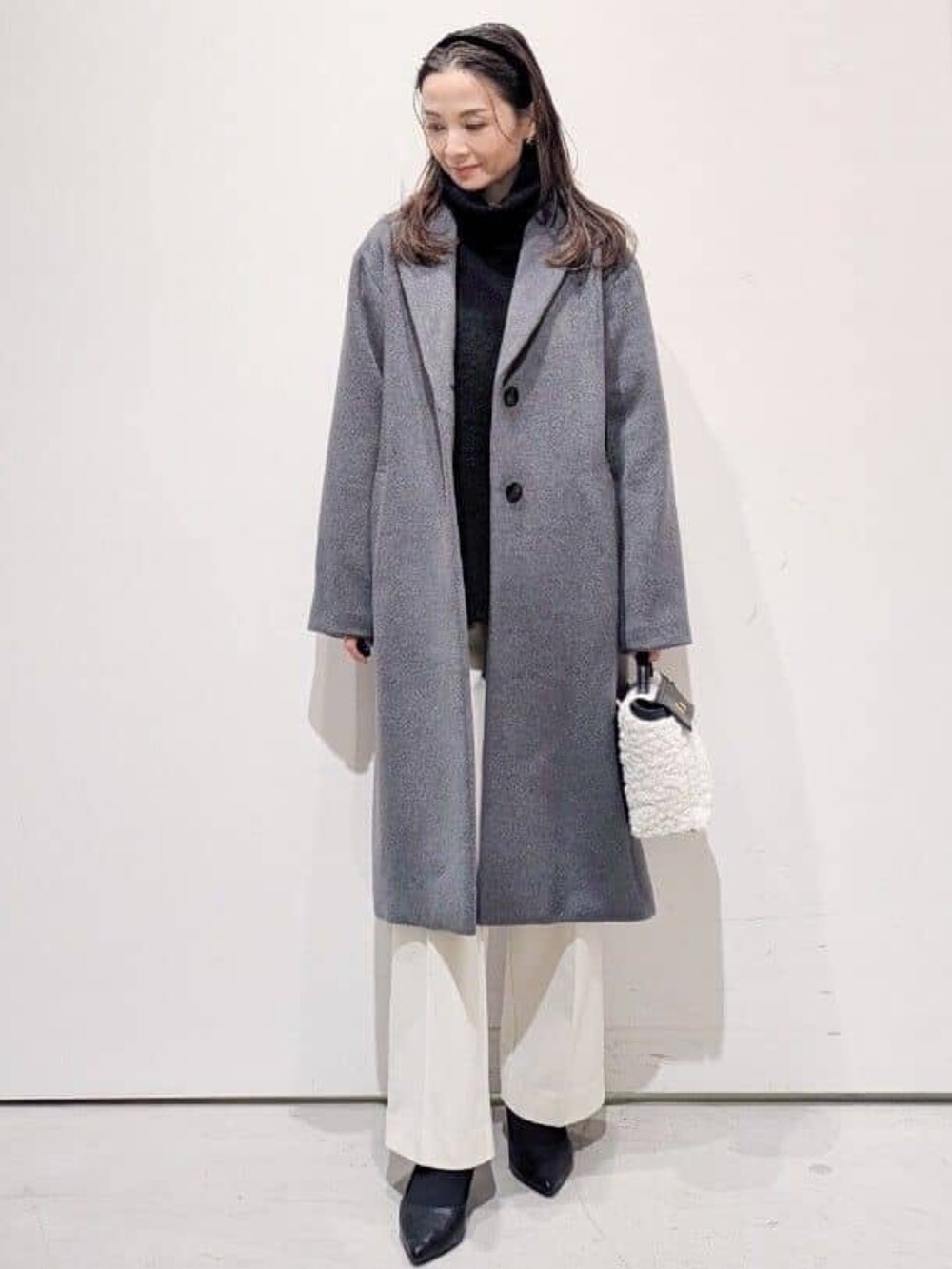 グレー系のチェスターコート、ホワイト系のその他パンツ、ブラック系のニット/セーターを着用したレディースの冬コーディネートの2枚目の写真