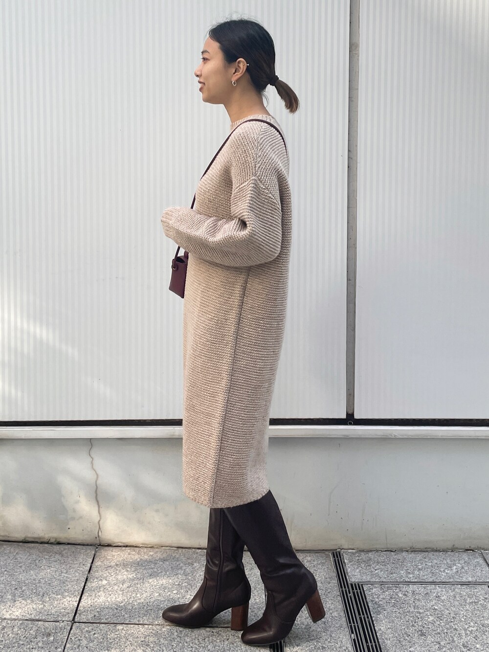 ベージュ系のワンピース、レッド系のショルダーバッグ、ブラウン系のブーツを着用したレディースの冬コーディネートの2枚目の写真