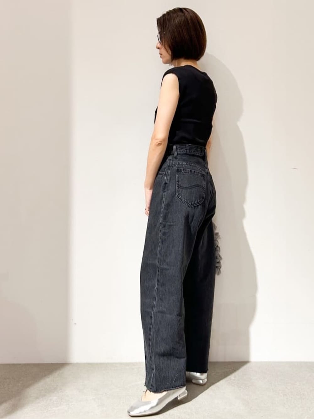 ブラック系のニット/セーター、グレー系のデニムパンツ、シルバー系のパンプスを着用したレディースの夏コーディネートの4枚目の写真