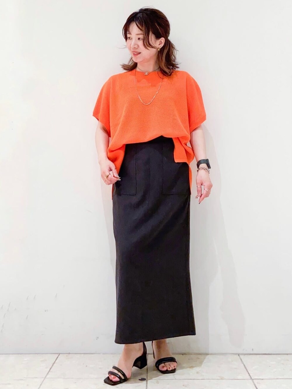 オレンジ系のニット/セーター、グレー系のスカート、ブラック系のショルダーバッグを着用したレディースの夏コーディネートの5枚目の写真