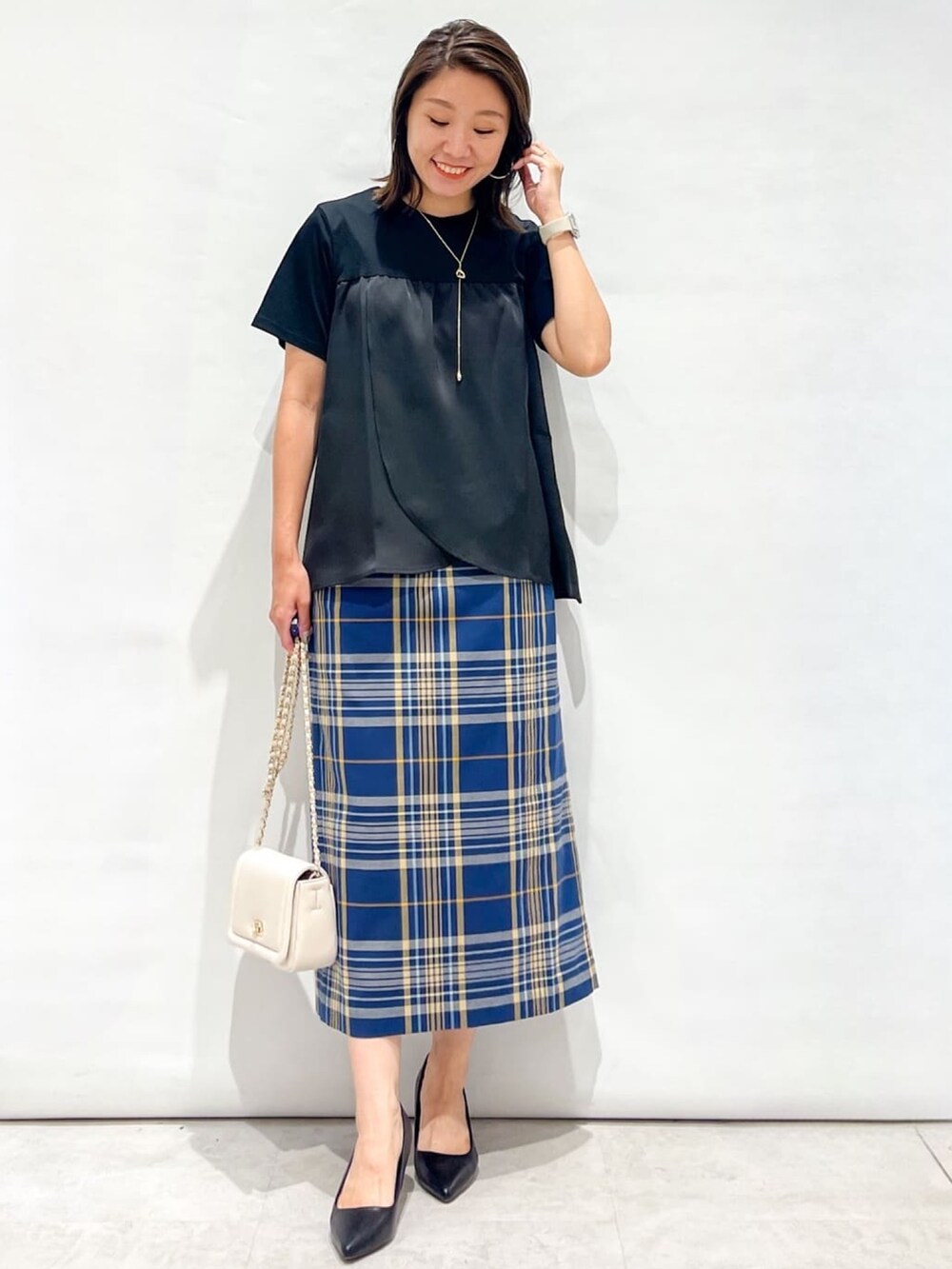 ブルー系のスカート、ブラック系のパンプス、ホワイト系のショルダーバッグを着用したレディースの夏コーディネートの2枚目の写真