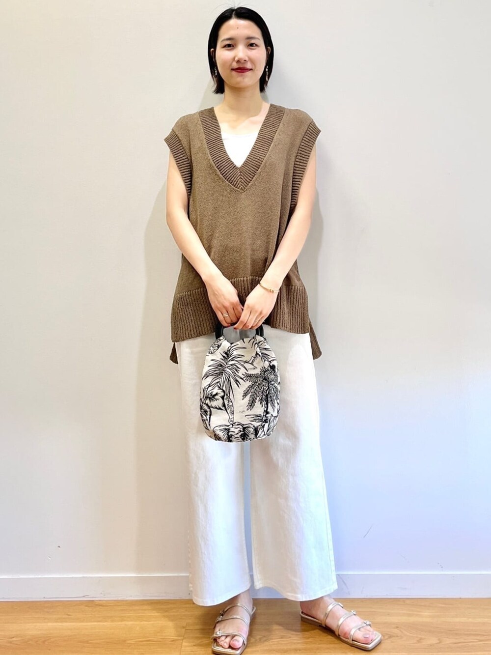 グリーン系のベスト、ホワイト系のハンドバッグ、ホワイト系のデニムパンツを着用したレディースの春コーディネートの2枚目の写真