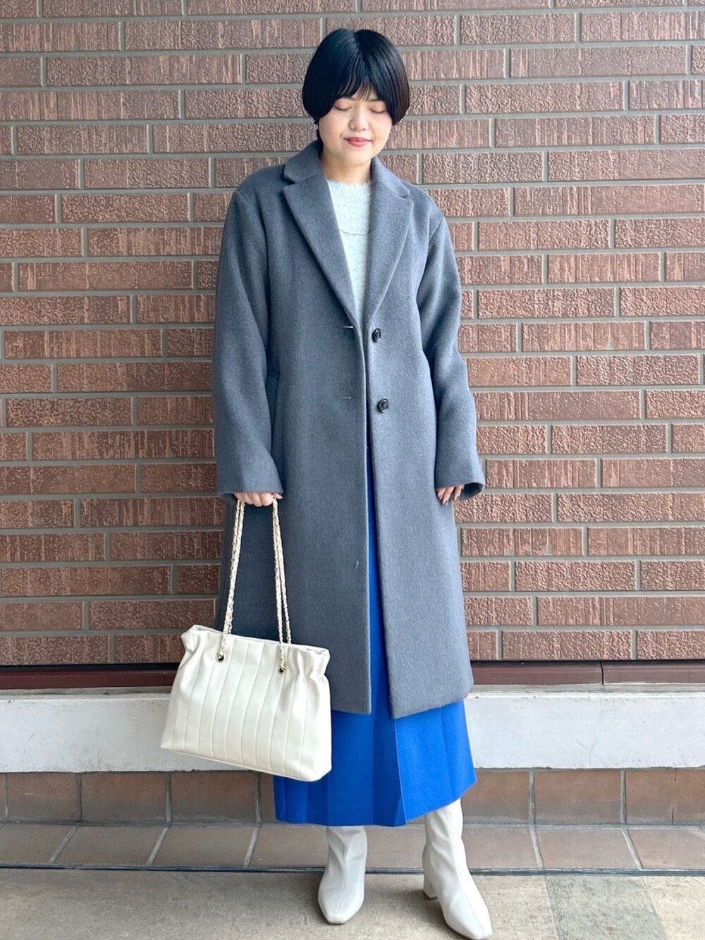 ブルー系のスカート、グレー系のニット/セーター、グレー系のチェスターコートを着用したレディースの秋コーディネートの2枚目の写真