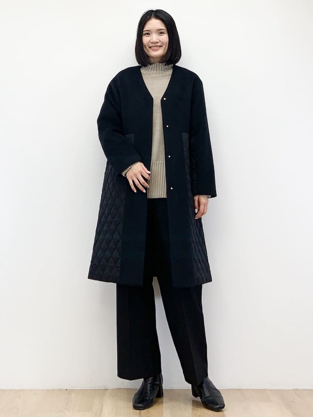 ブラック系のノーカラーコート、ベージュ系のニット/セーター、ブラック系のその他パンツを着用したレディースの秋コーディネートの2枚目の写真