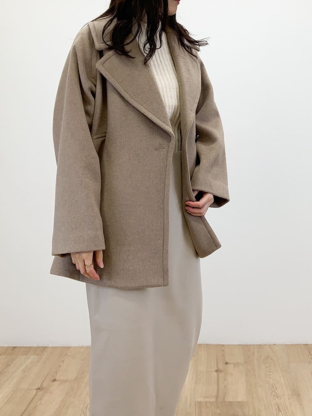 ブラウン系のピーコート、ベージュ系のスカート、ホワイト系のニット/セーターを着用したレディースの冬コーディネートの3枚目の写真