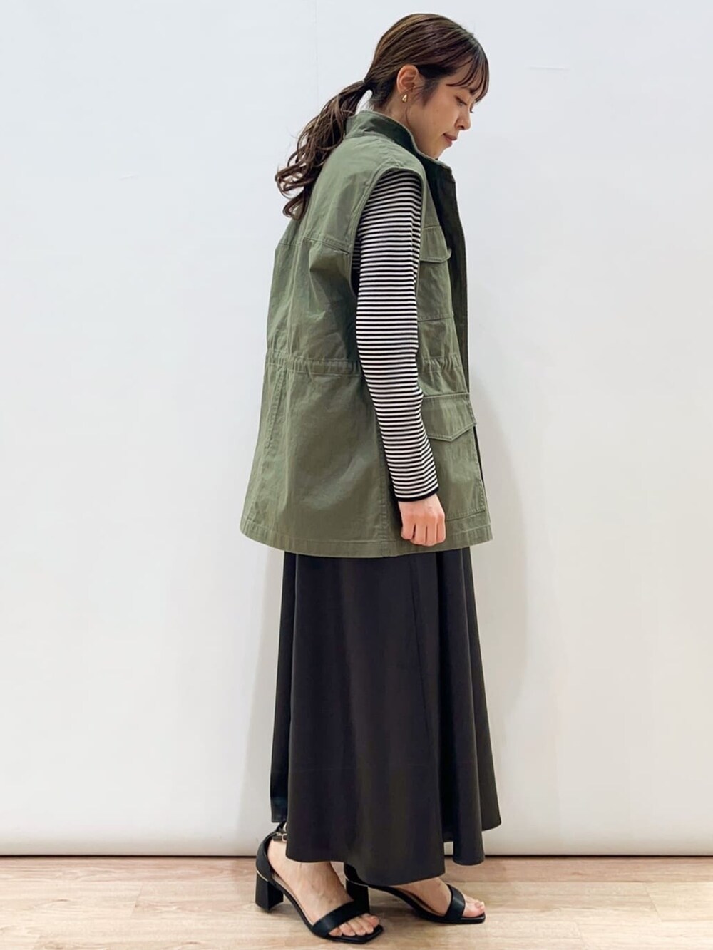 グレー系のワンピース、ブラック系のサンダル、ホワイト系のニット/セーターを着用したレディースの春コーディネートの2枚目の写真