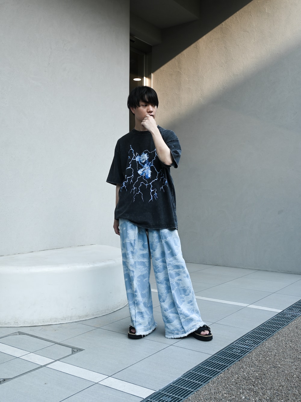 ブラック系のTシャツ/カットソー、ブルー系のデニムパンツ、ブラック系のサンダルを着用したメンズの夏コーディネートの2枚目の写真
