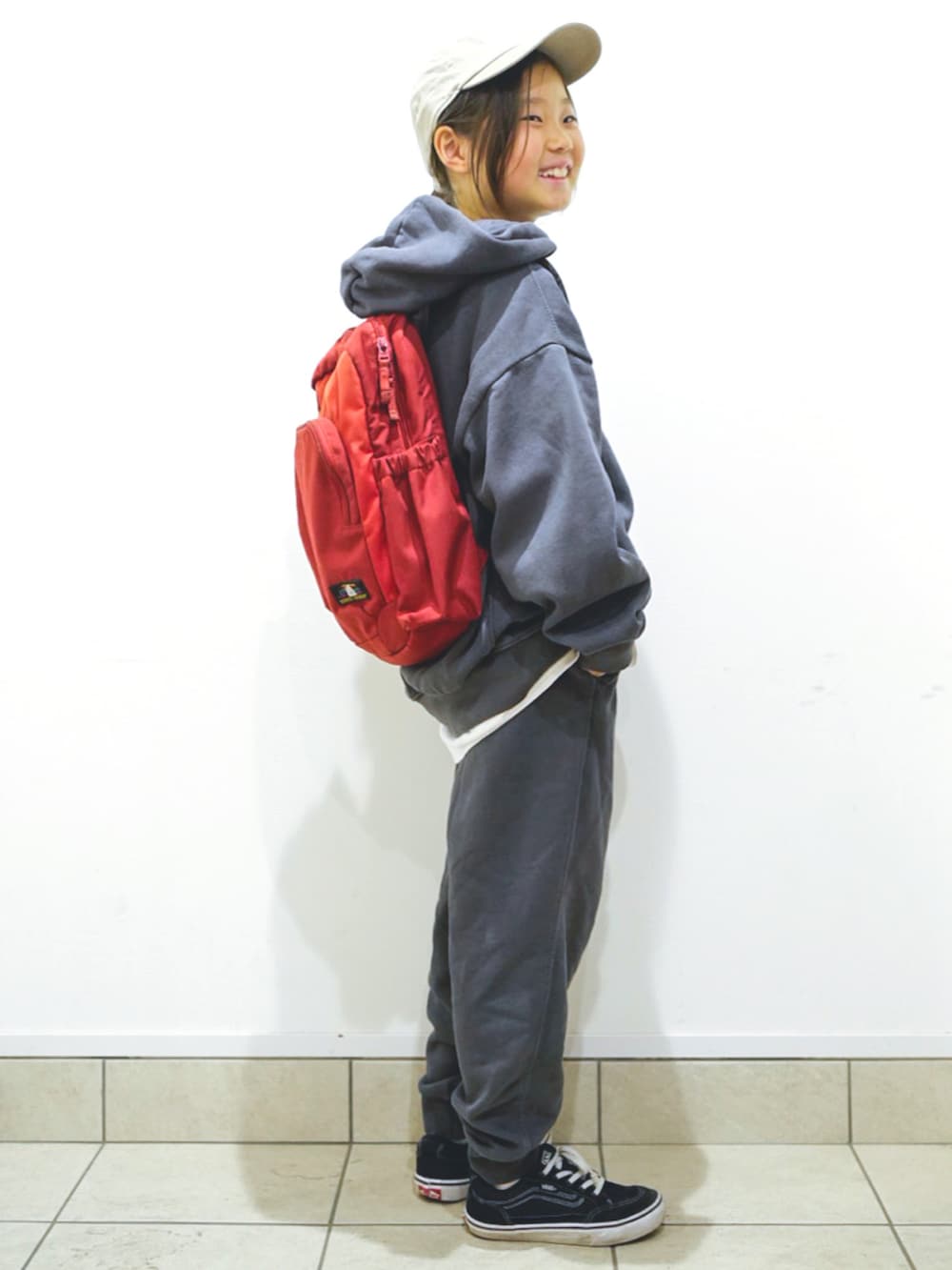 グレー系のパーカー、ブラック系のスニーカー、レッド系のバックパック/リュックを着用したキッズの春コーディネートの2枚目の写真