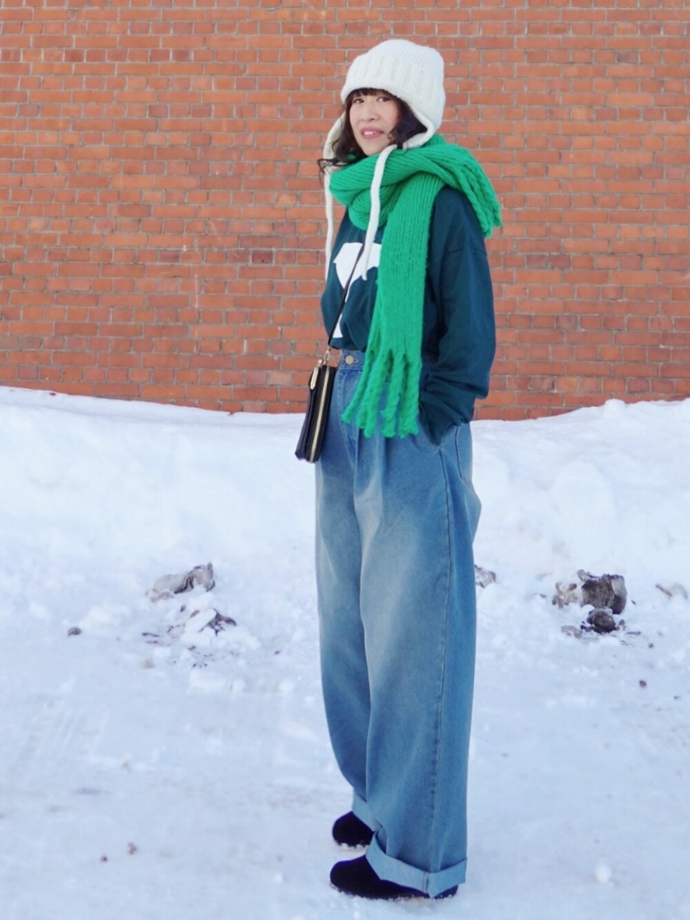 グリーン系のスウェット、ブラック系のショルダーバッグ、ブルー系のデニムパンツを着用したレディースの冬コーディネートの2枚目の写真