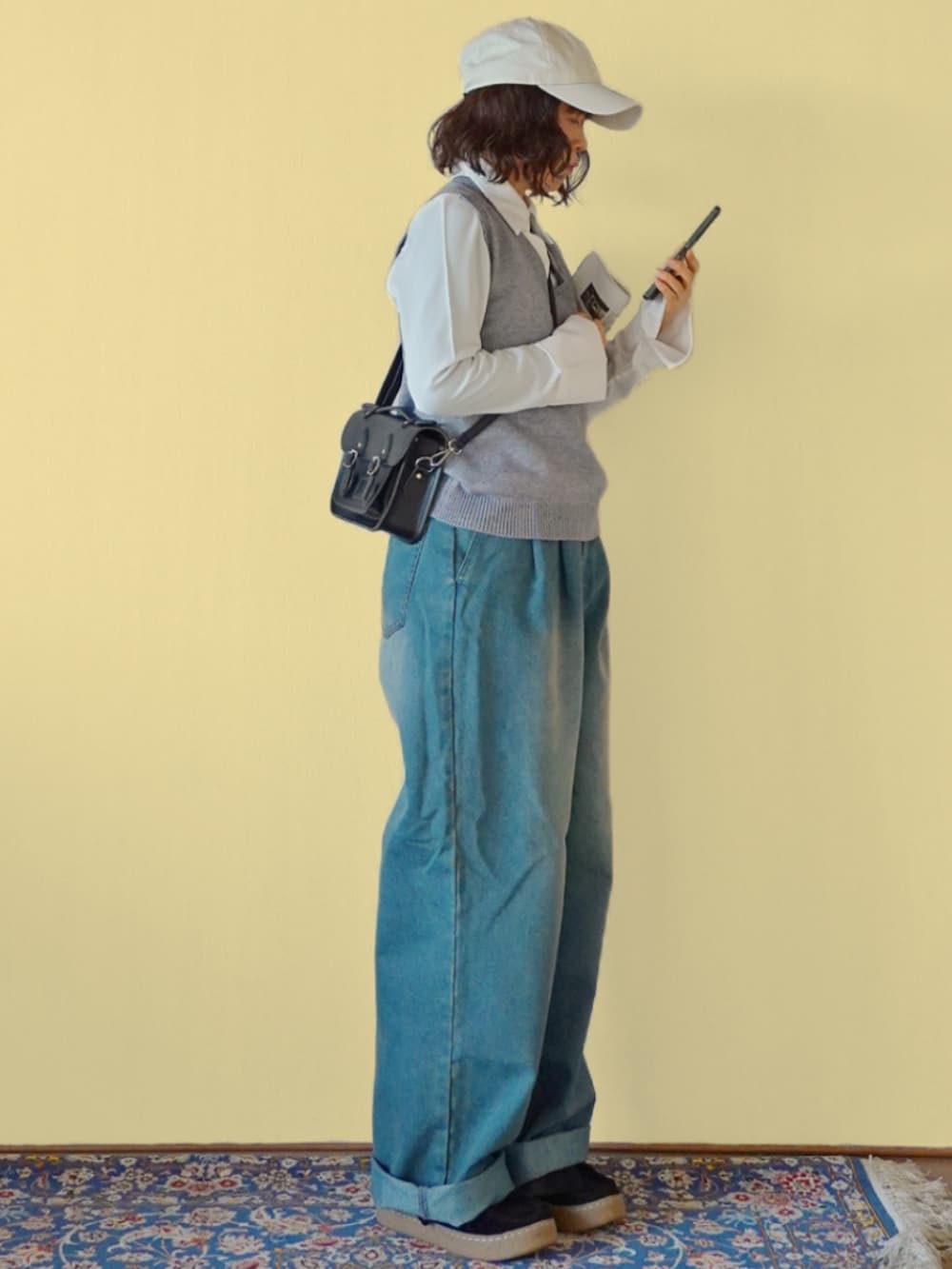 グレー系のベスト、ブルー系のデニムパンツ、ブラック系のショルダーバッグを着用したレディースの冬コーディネートの2枚目の写真