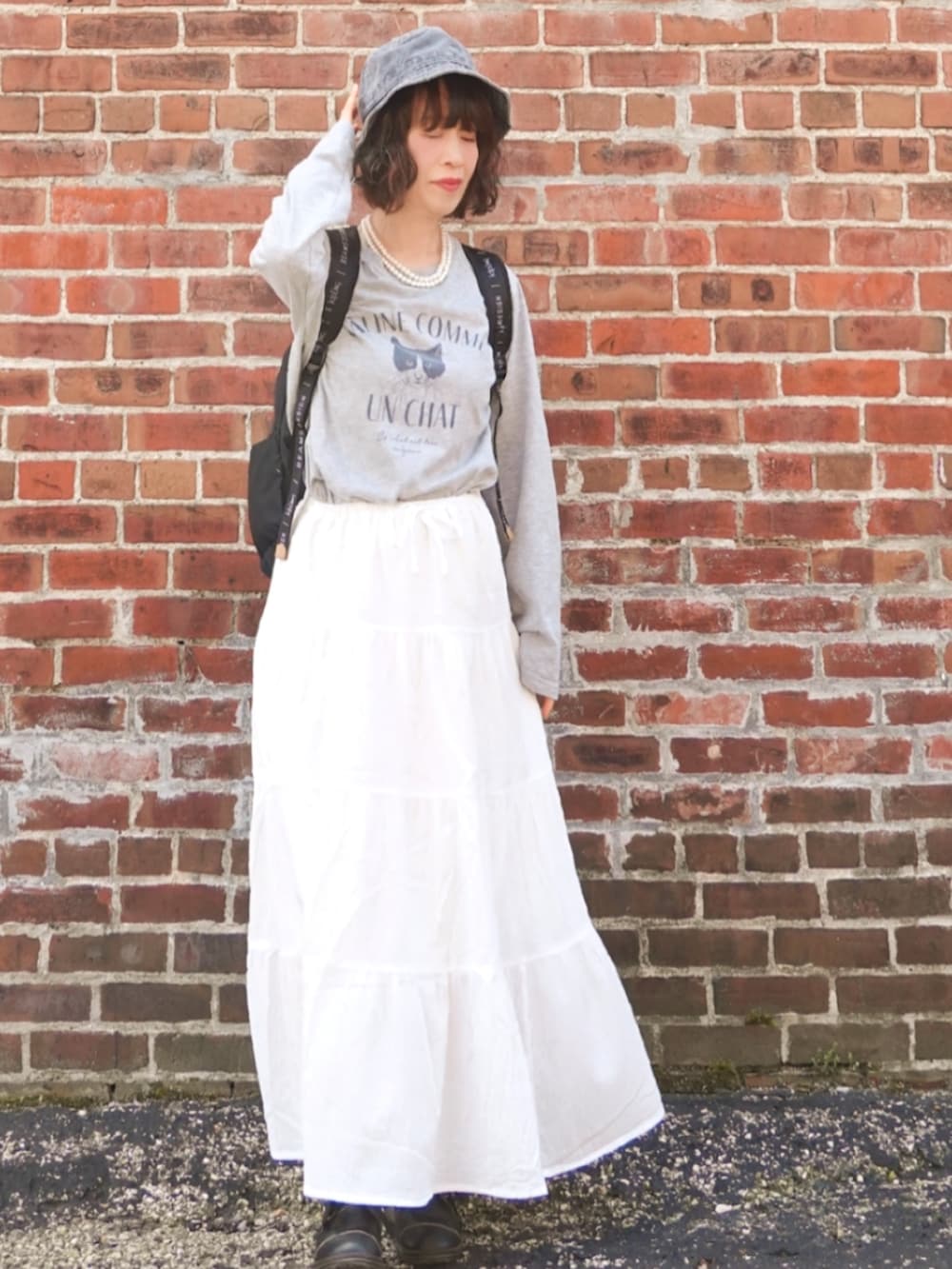 グレー系のTシャツ/カットソー、ホワイト系のスカート、ブラック系のバックパック/リュックを着用したレディースの春コーディネートの2枚目の写真