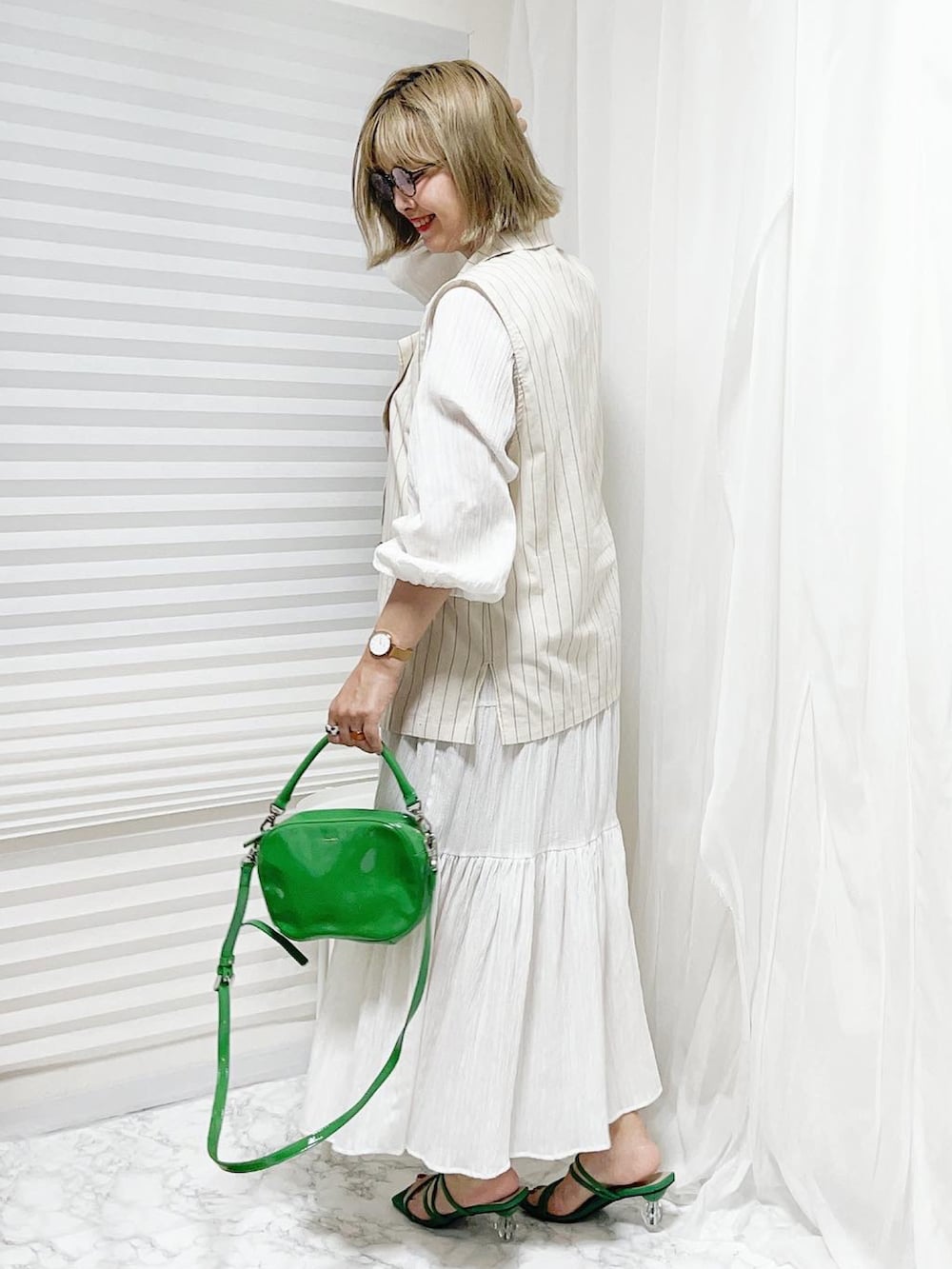 ホワイト系のベスト、グリーン系のショルダーバッグ、ホワイト系のワンピースを着用したレディースの春コーディネートの2枚目の写真