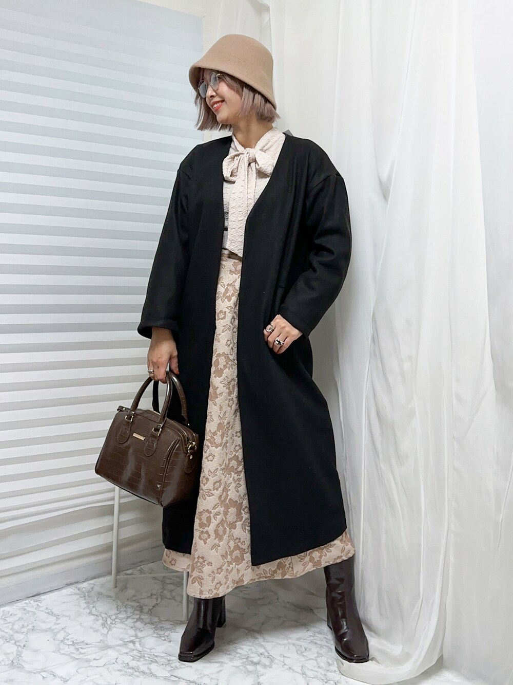 ブラウン系のボストンバッグ、ブラウン系のブーツ、ブラック系のノーカラーコートを着用したレディースの冬コーディネートの2枚目の写真