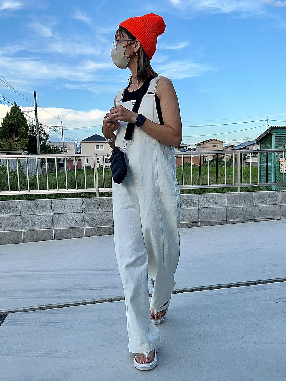 ホワイト系のサロペット/オーバーオール、ホワイト系のサンダル、オレンジ系のニットキャップ/ビーニーを着用したレディースの秋コーディネートの3枚目の写真