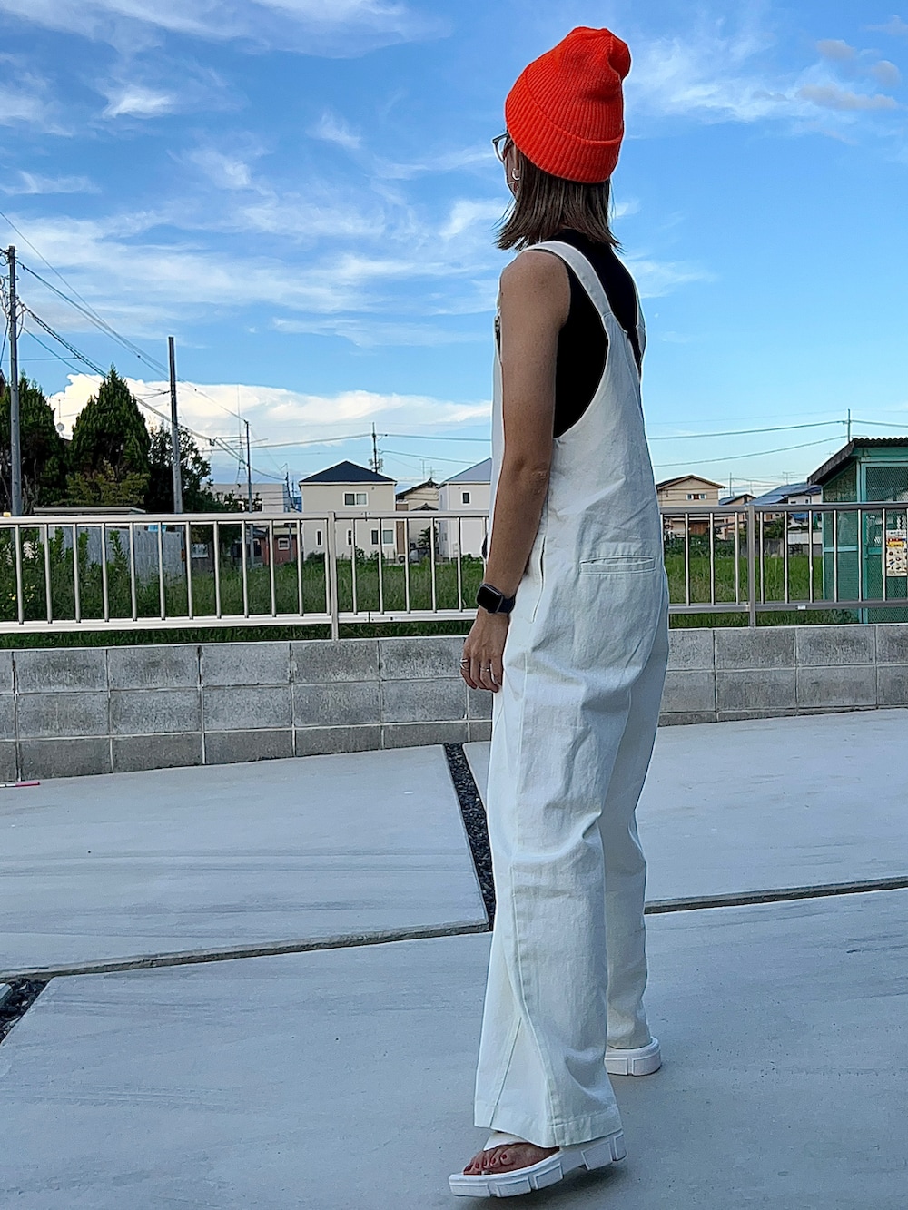 ホワイト系のサロペット/オーバーオール、ホワイト系のサンダル、オレンジ系のニットキャップ/ビーニーを着用したレディースの秋コーディネートの2枚目の写真
