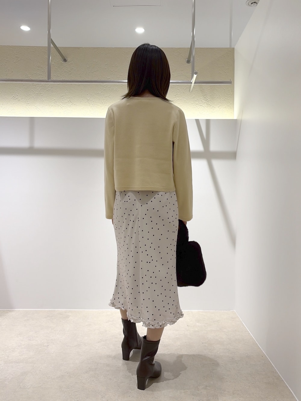 イエロー系のカーディガン/ボレロ、ホワイト系のスカート、ブラウン系のブーツを着用したレディースの秋コーディネートの3枚目の写真