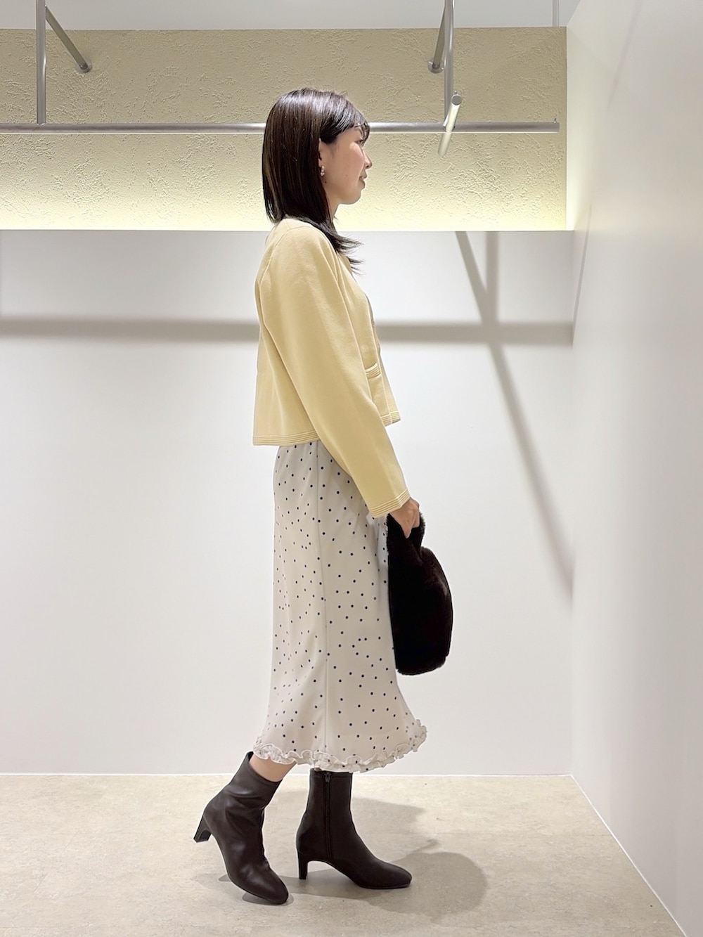 イエロー系のカーディガン/ボレロ、ホワイト系のスカート、ブラウン系のブーツを着用したレディースの秋コーディネートの4枚目の写真