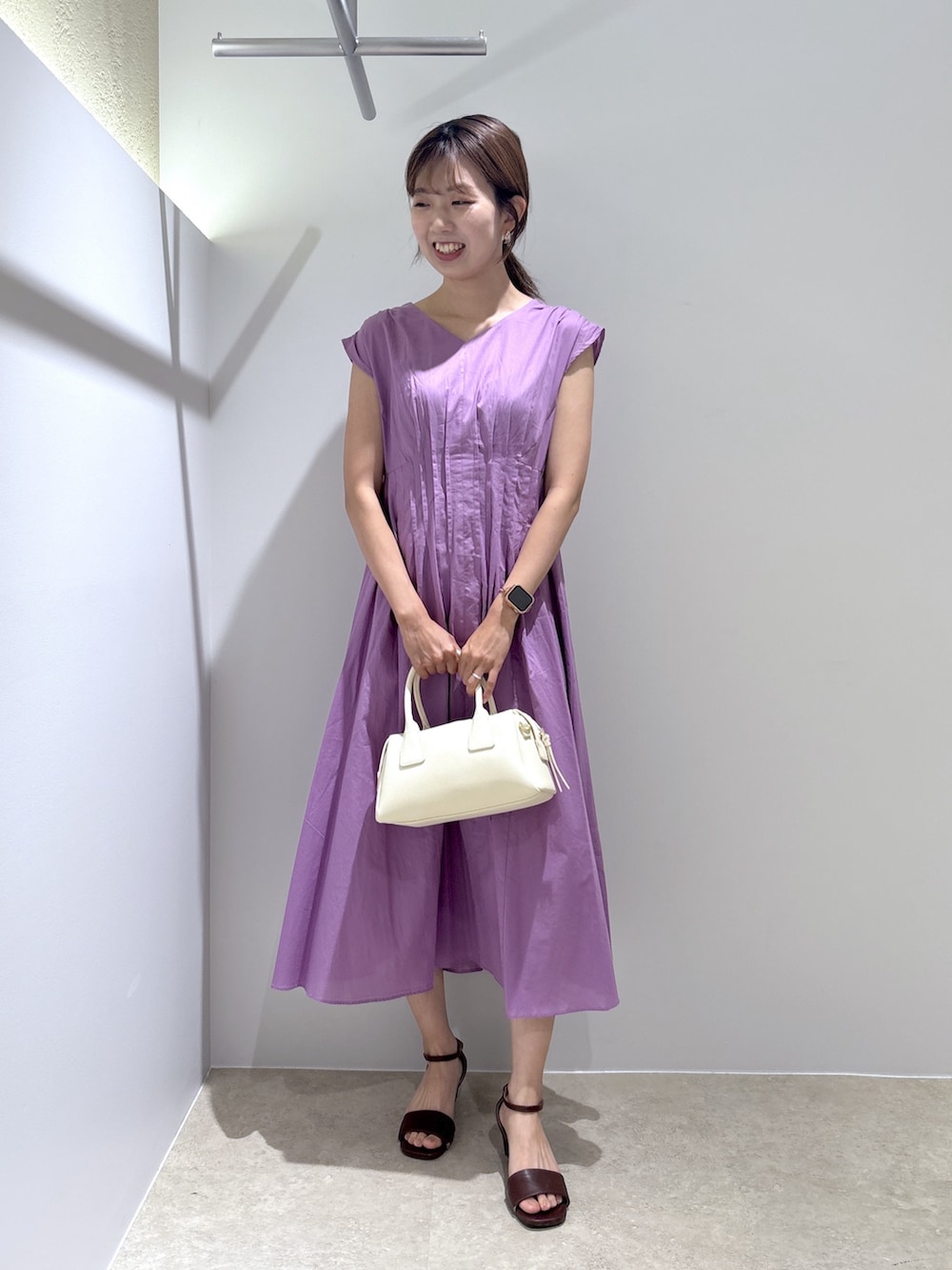 パープル系のワンピース、ホワイト系のボストンバッグ、ブラウン系のサンダルを着用したレディースの夏コーディネートの2枚目の写真