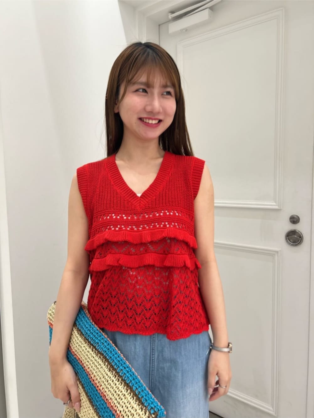 ブルー系のトートバッグ、レッド系のニット/セーター、ブルー系のデニムパンツを着用したレディースの春コーディネートの5枚目の写真