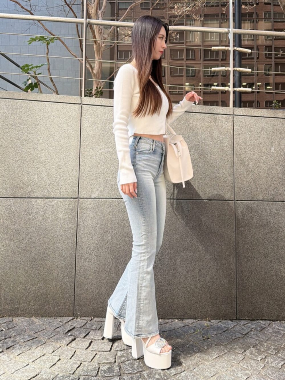 ブルー系のデニムパンツ、ホワイト系のサンダル、ホワイト系のハンドバッグを着用したレディースの春コーディネートの2枚目の写真