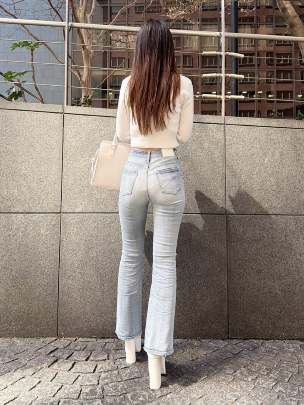 ブルー系のデニムパンツ、ホワイト系のサンダル、ホワイト系のハンドバッグを着用したレディースの春コーディネートの3枚目の写真