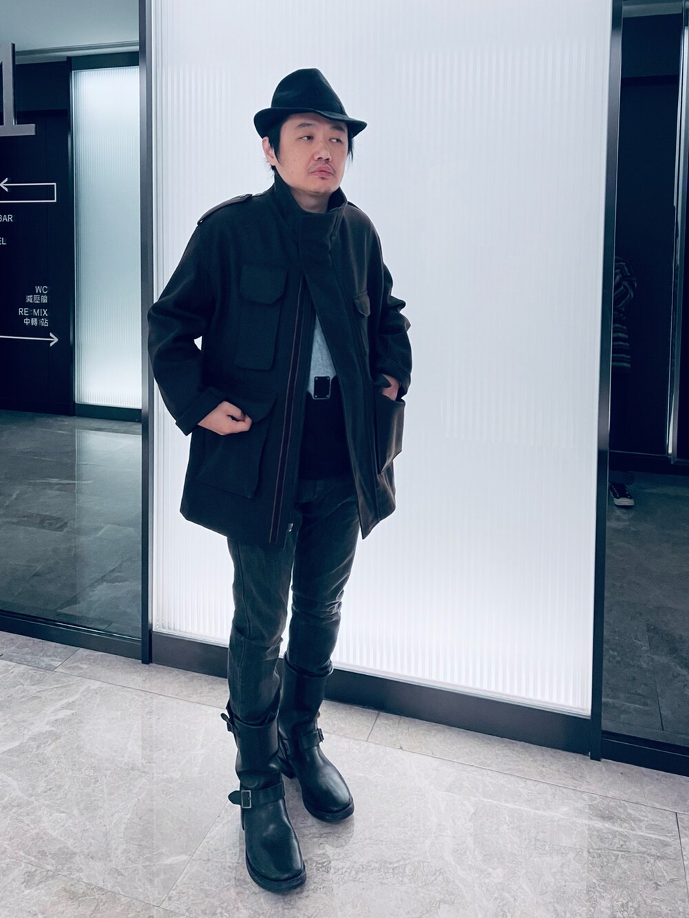 ブラック系のTシャツ/カットソー、ブラウン系のノーカラーコート、ブラック系のブーツを着用したメンズの冬コーディネートの2枚目の写真