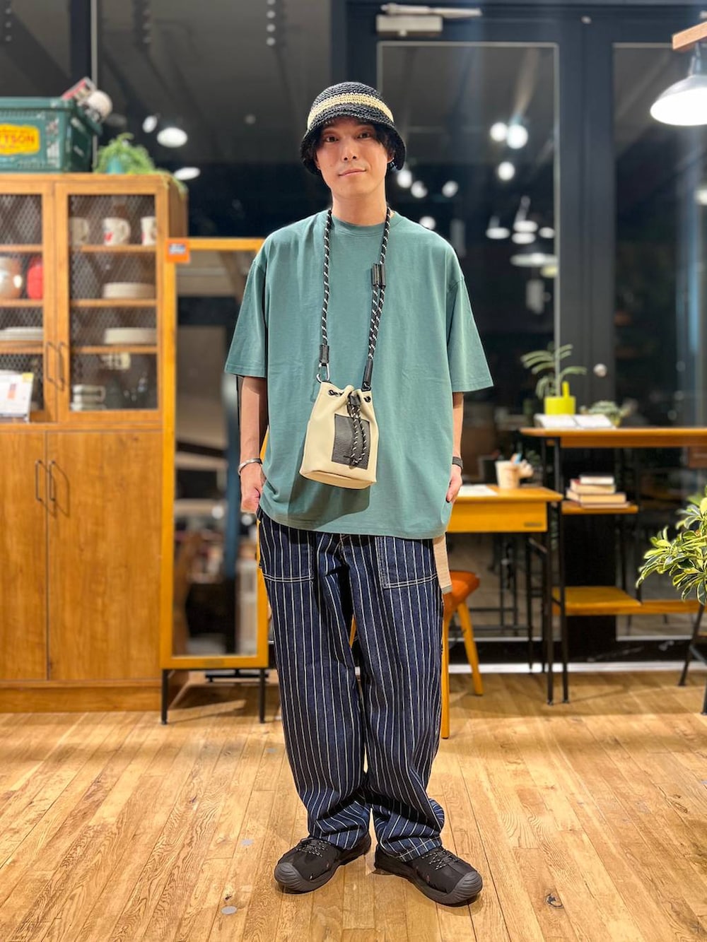 グレー系のショルダーバッグ、グリーン系のTシャツ/カットソー、ブラック系のサンダルを着用したメンズの夏コーディネートの2枚目の写真