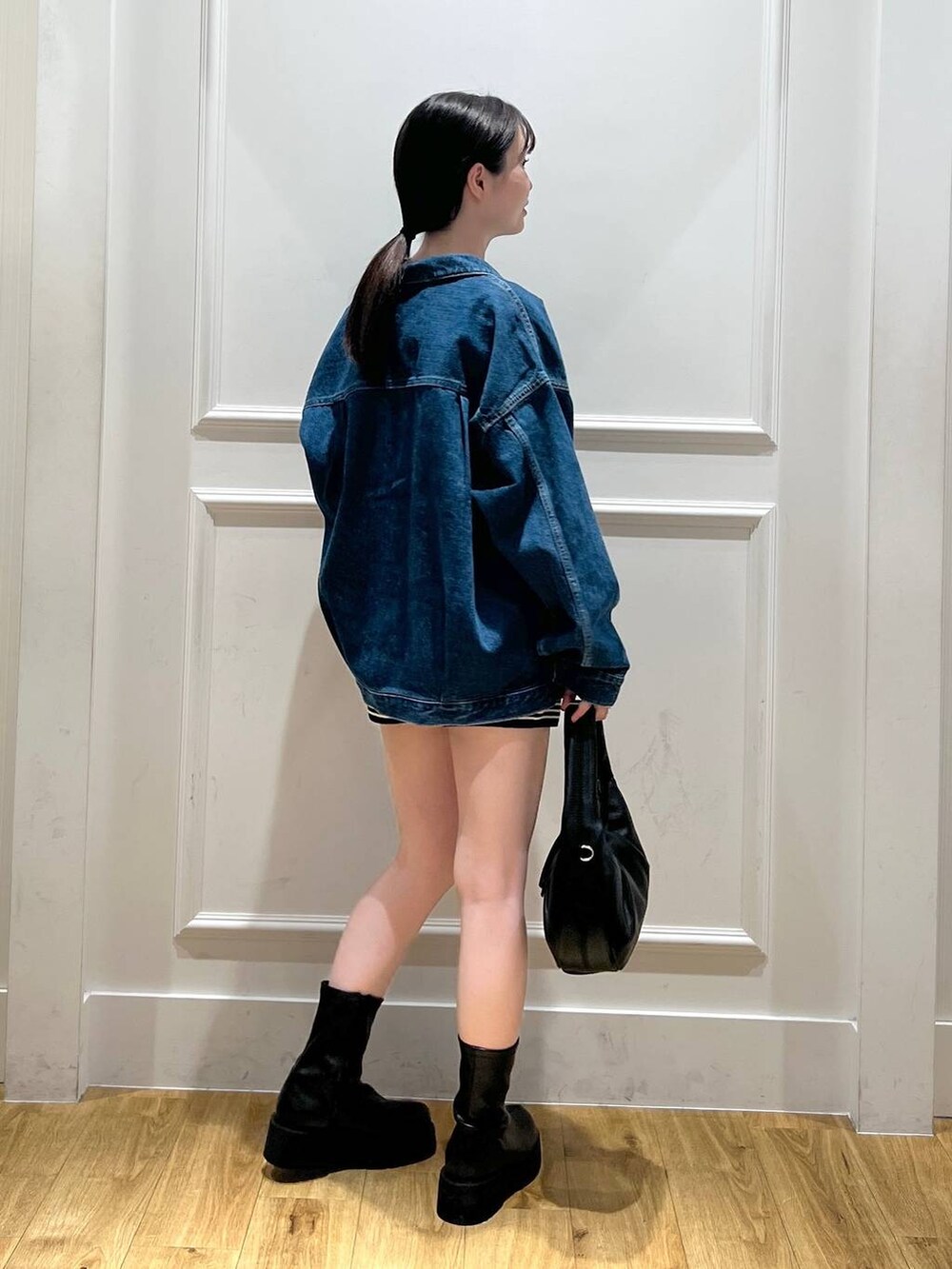 ブラック系のハンドバッグ、ブルー系のデニムジャケット、ブラック系のブーツを着用したレディースの秋コーディネートの3枚目の写真