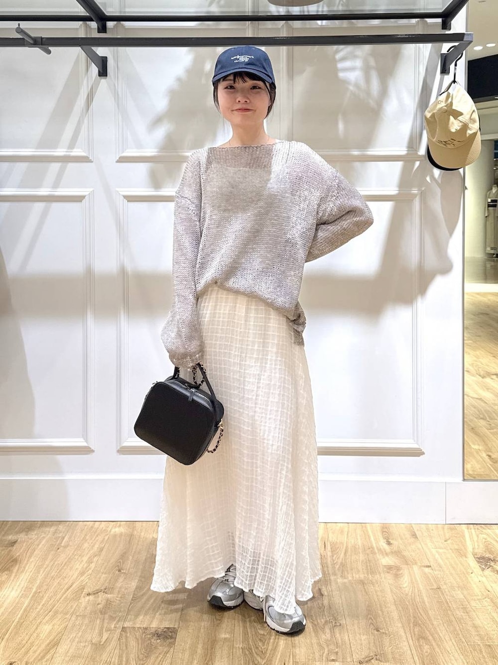 グレー系のニット/セーター、ブラック系のショルダーバッグ、ホワイト系のスカートを着用したレディースの春コーディネートの5枚目の写真
