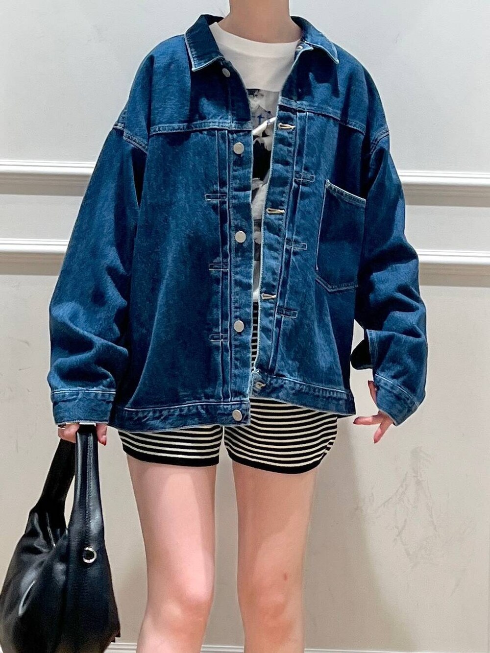 ブラック系のハンドバッグ、ブルー系のデニムジャケット、ブラック系のブーツを着用したレディースの秋コーディネートの2枚目の写真