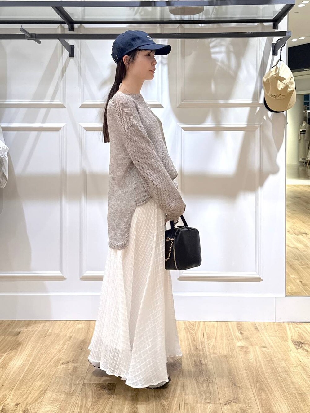 グレー系のニット/セーター、ブラック系のショルダーバッグ、ホワイト系のスカートを着用したレディースの春コーディネートの4枚目の写真