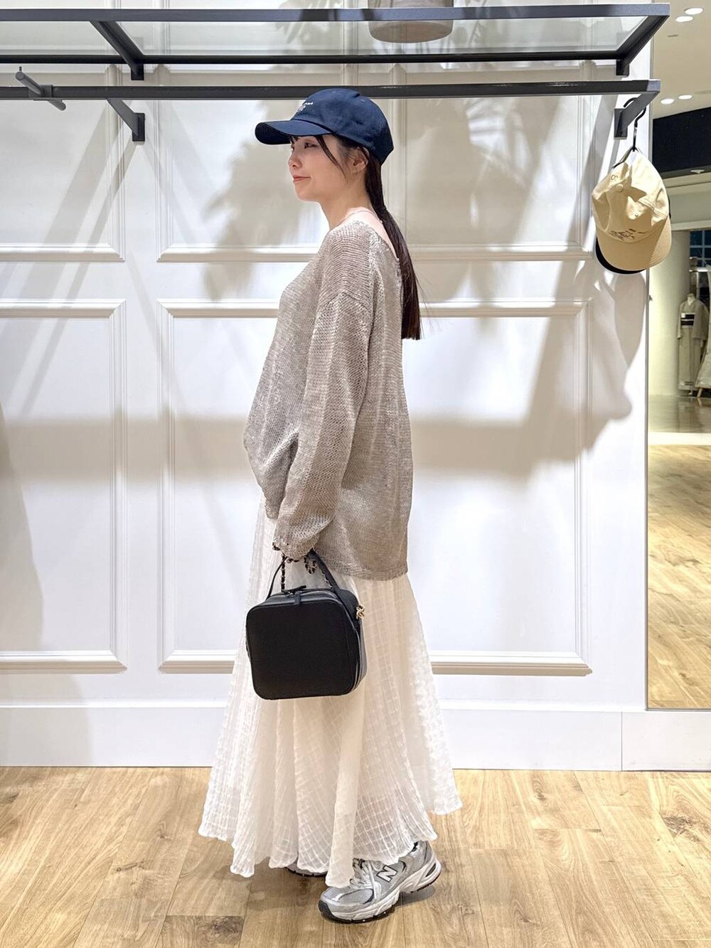 グレー系のニット/セーター、ブラック系のショルダーバッグ、ホワイト系のスカートを着用したレディースの春コーディネートの2枚目の写真