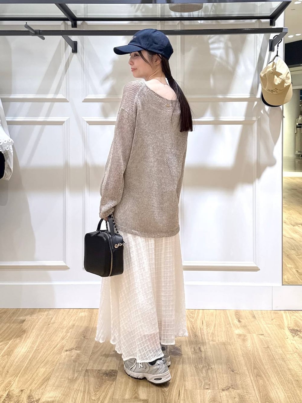 グレー系のニット/セーター、ブラック系のショルダーバッグ、ホワイト系のスカートを着用したレディースの春コーディネートの3枚目の写真