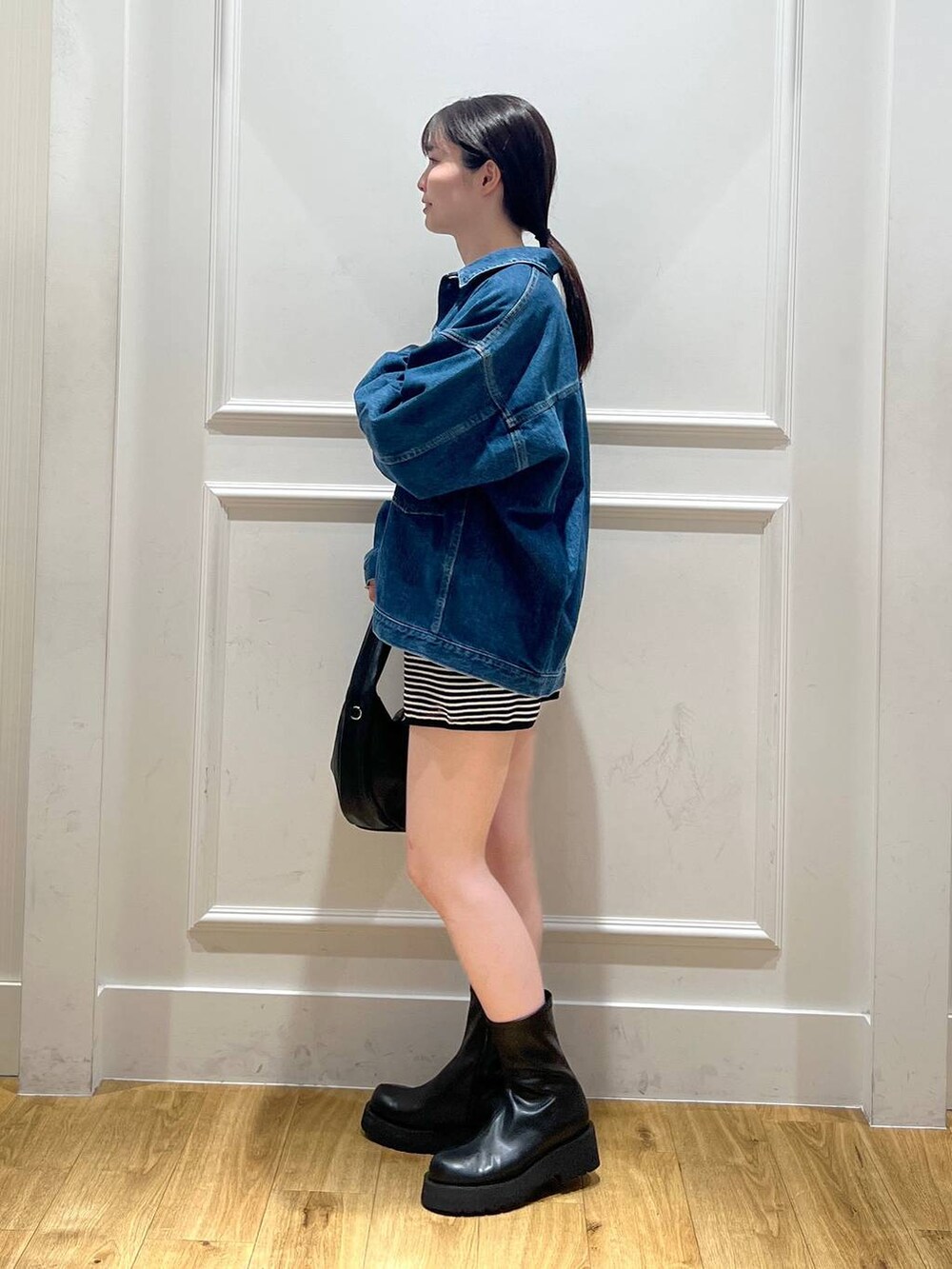 ブラック系のハンドバッグ、ブルー系のデニムジャケット、ブラック系のブーツを着用したレディースの秋コーディネートの4枚目の写真