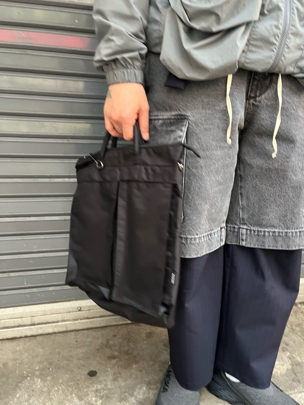 グレー系のパンツ、ブラック系のショルダーバッグ、ブラック系のスリッポンを着用したメンズの春コーディネートの3枚目の写真