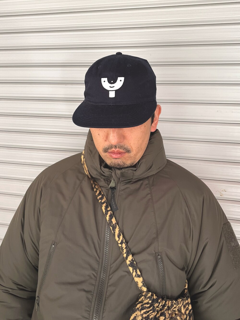 グリーン系のダウンジャケット/コート、ゴールド系のバッグ、ブルー系のキャップを着用したメンズの冬コーディネートの2枚目の写真