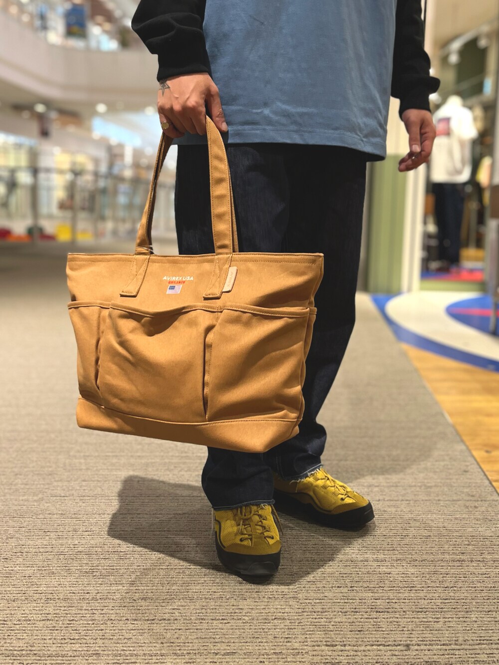 ブラウン系のトートバッグ、グレー系のTシャツ/カットソー、グリーン系のハットを着用したメンズの夏コーディネートの3枚目の写真