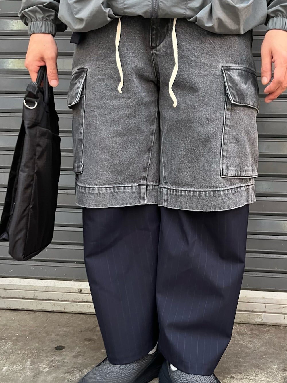 グレー系のパンツ、ブラック系のショルダーバッグ、ブラック系のスリッポンを着用したメンズの春コーディネートの4枚目の写真