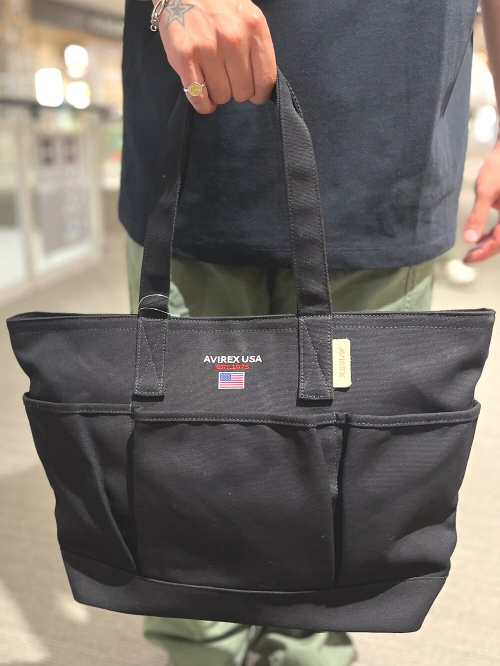 ブラック系のトートバッグ、ブラック系のTシャツ/カットソー、グリーン系のカーゴパンツを着用したメンズの夏コーディネートの3枚目の写真