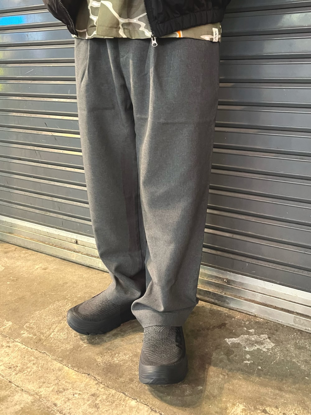 グレー系のスラックス、ブラック系のスニーカー、ホワイト系のナイロンジャケットを着用したメンズの春コーディネートの3枚目の写真