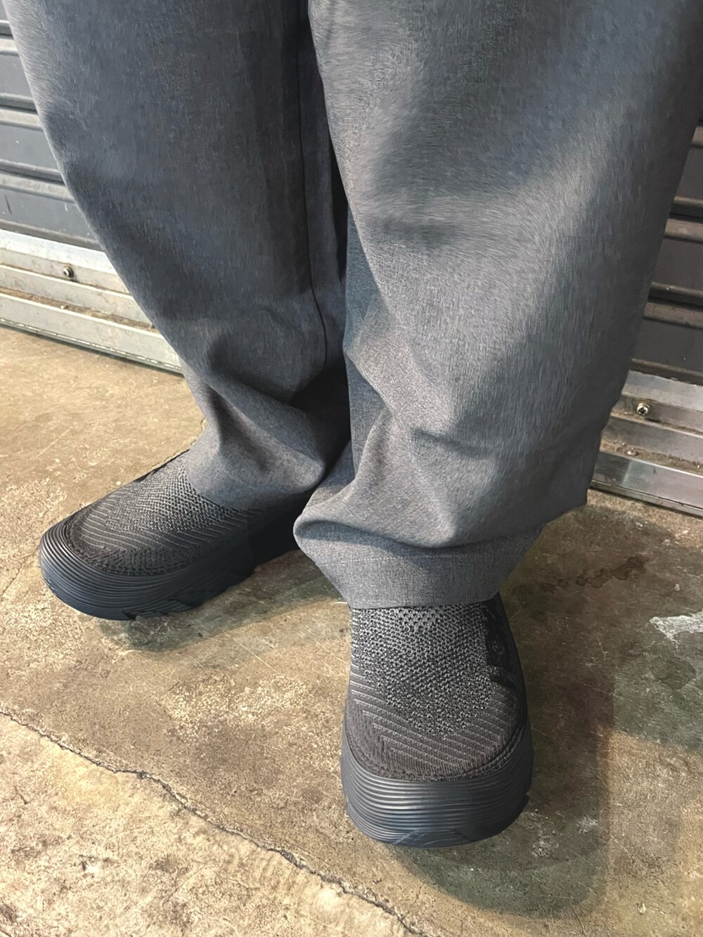 グレー系のスラックス、ブラック系のスニーカー、ホワイト系のナイロンジャケットを着用したメンズの春コーディネートの4枚目の写真