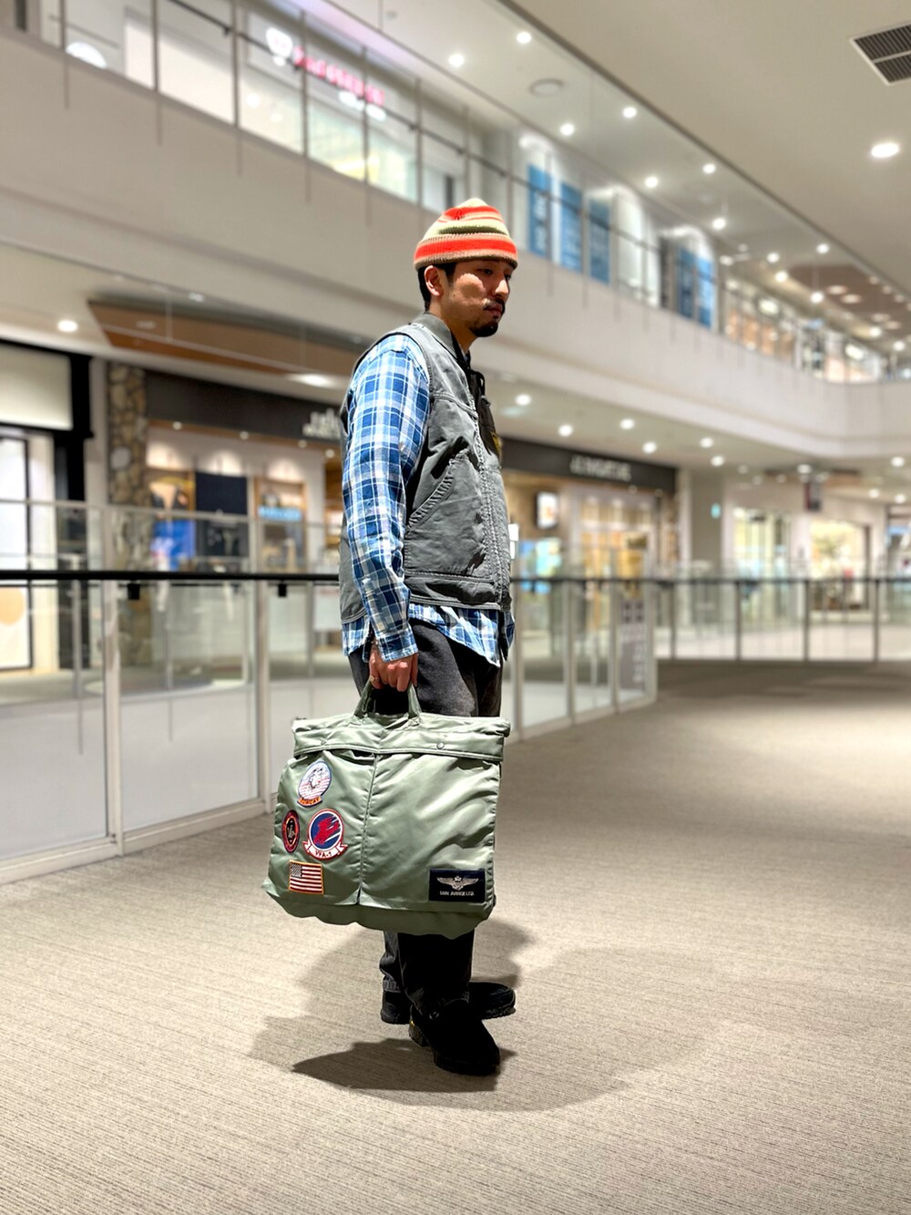 オレンジ系のシャツ/ブラウス、グリーン系のトートバッグ、ブラック系のベストを着用したメンズの冬コーディネートの2枚目の写真