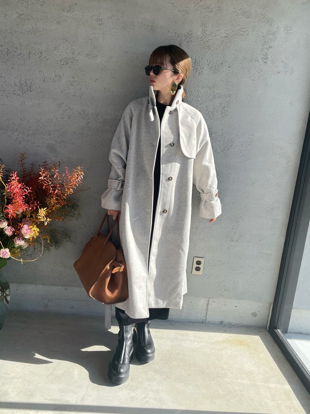 ベージュ系のトレンチコート、ブラウン系のハンドバッグ、ブラック系のブーツを着用したレディースの冬コーディネートの2枚目の写真